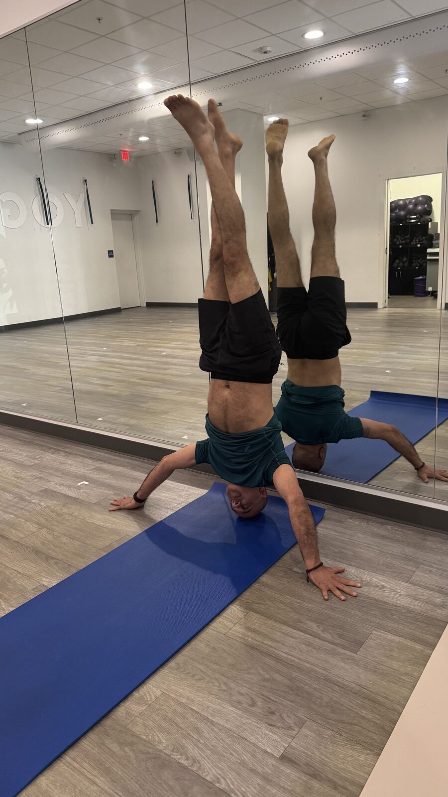 Raj in tripod headstand with legs scissored, wide view of the studio